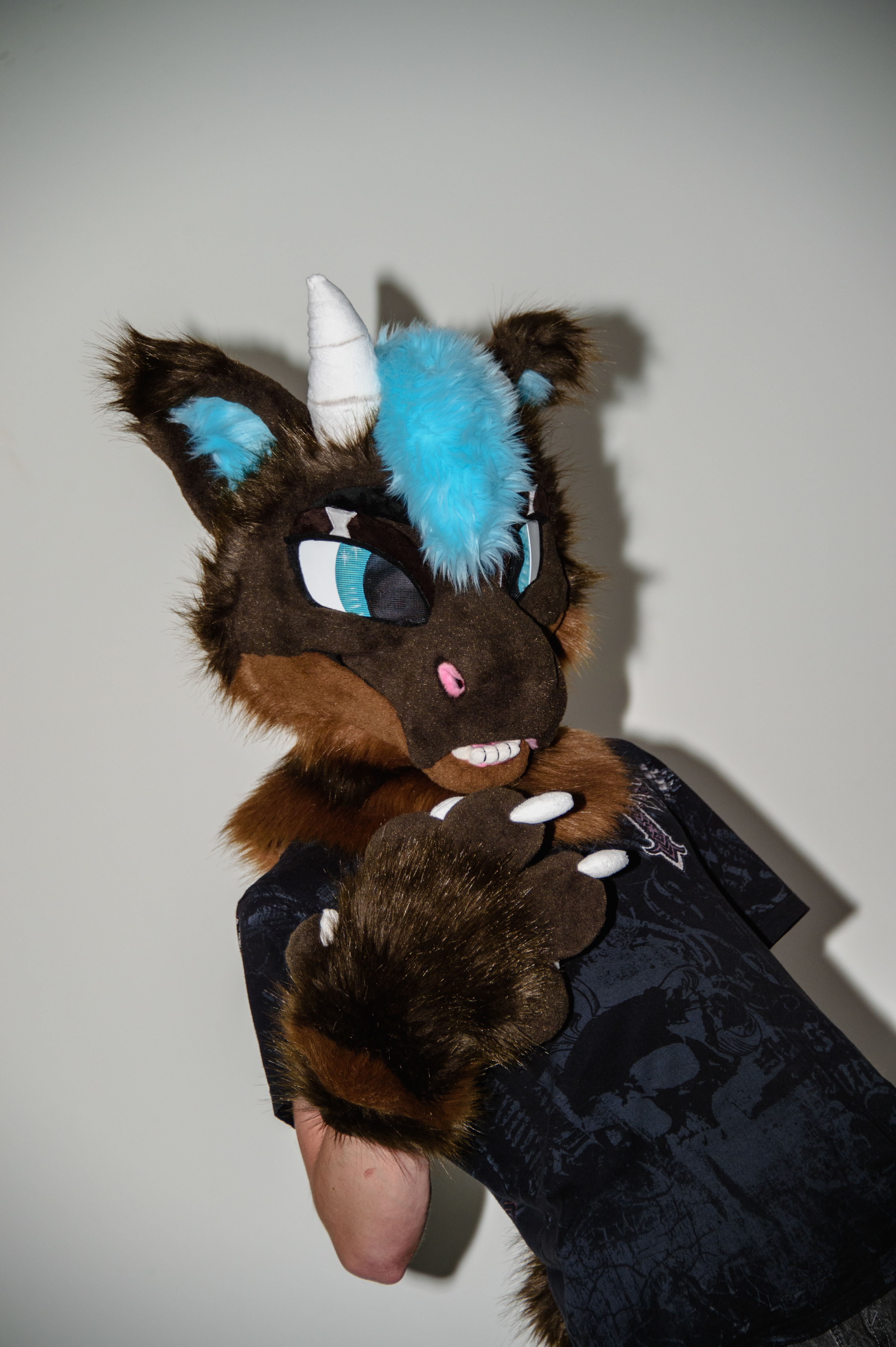 A person in a brown and blue fursuit posing up against a blank wall