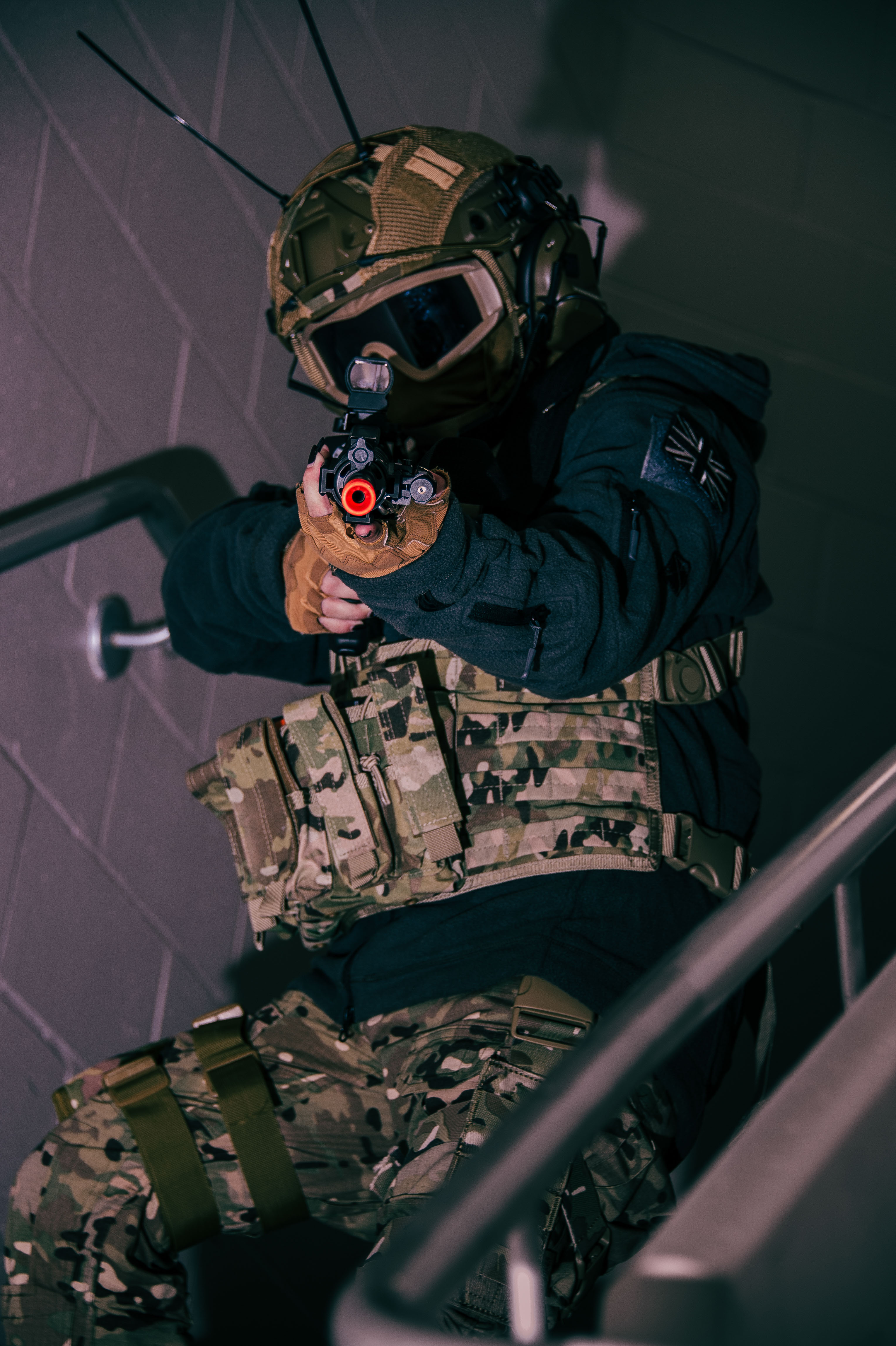A person dressed in tactical gear pointing a prop gun towards the camera while descending a staircase