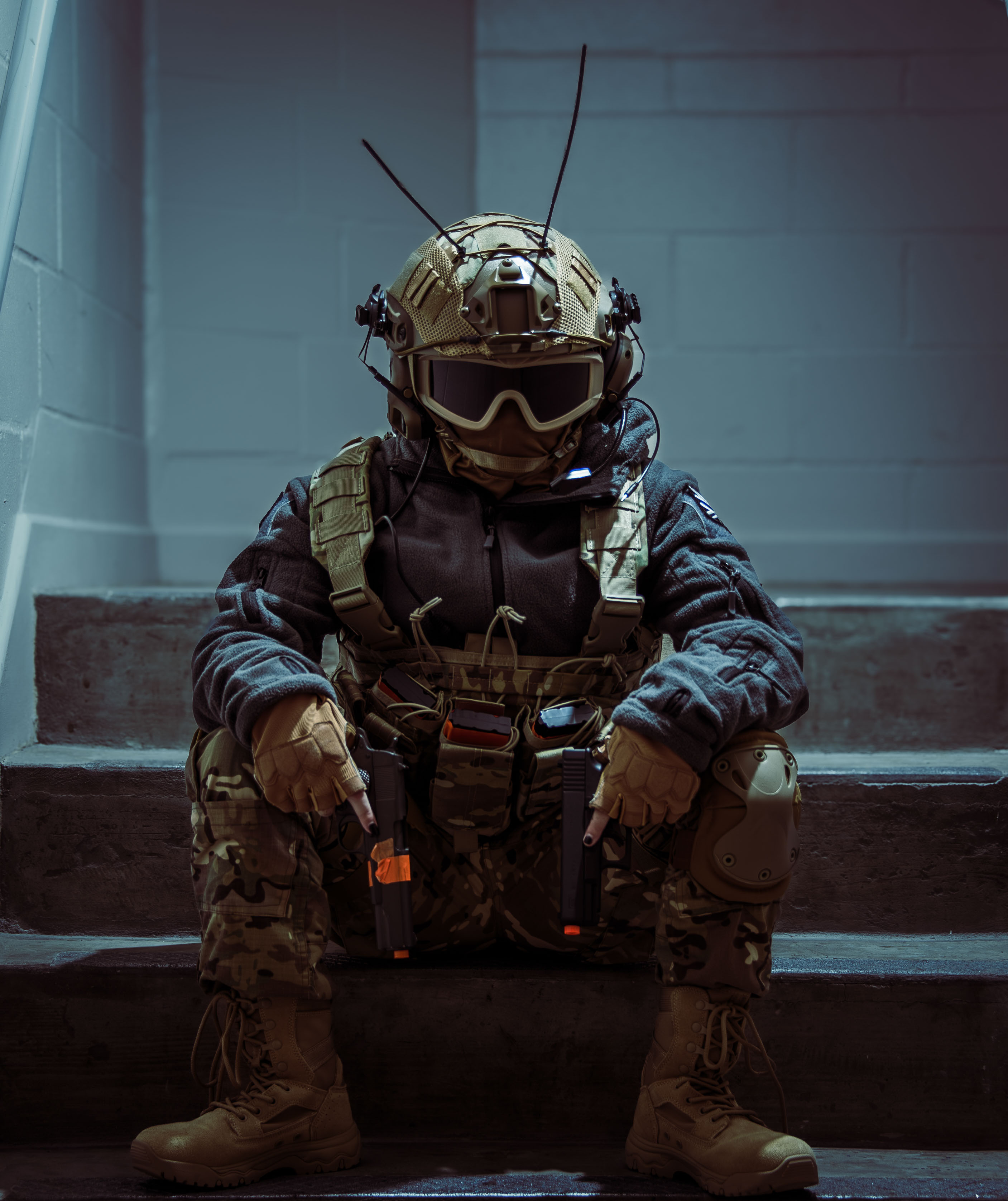 A person in full tactical gear sitting on the steps in a concrete/brutalist staircase