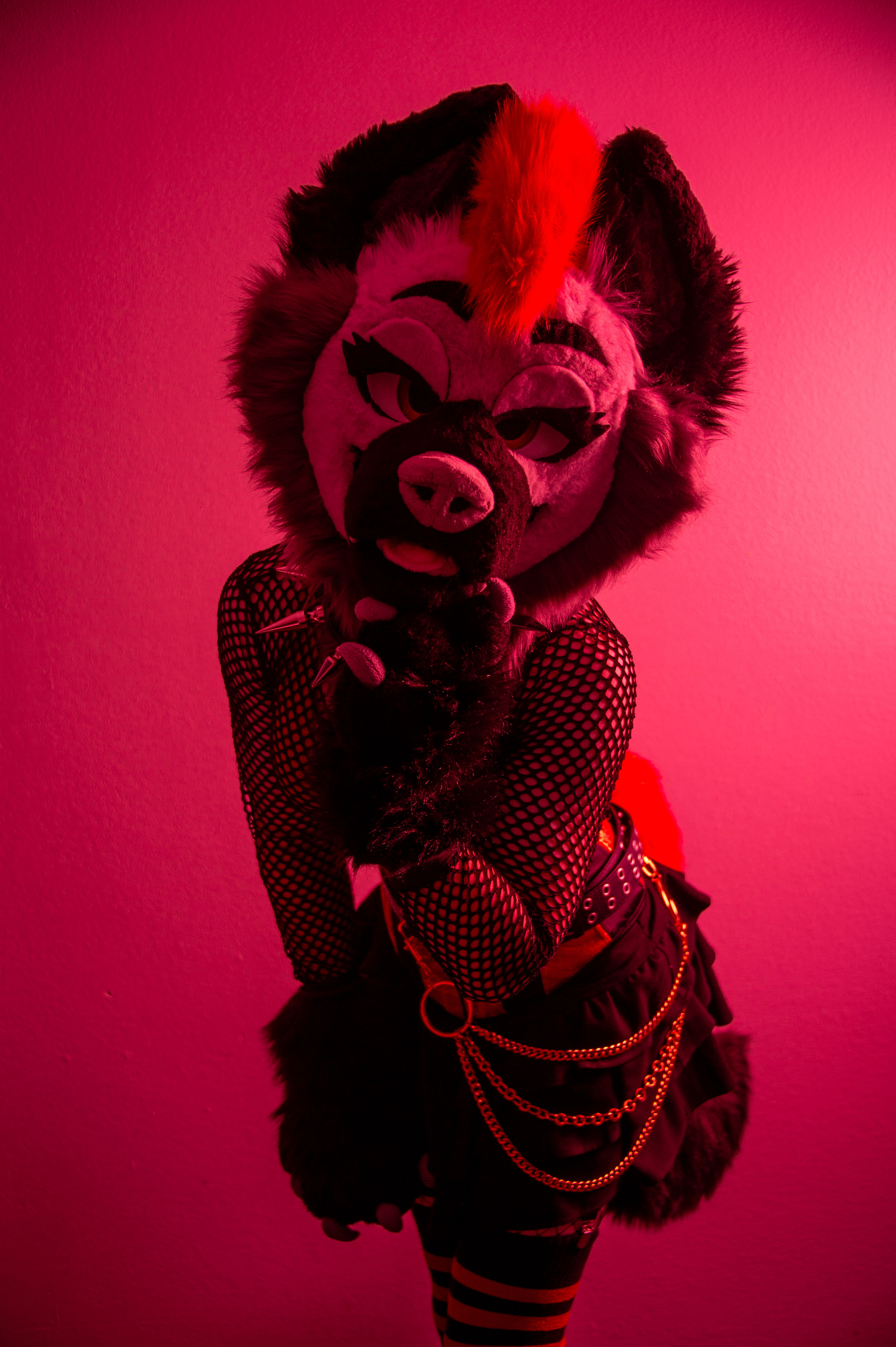 A person in a red, black, and grey fursuit illuminated by a red flash, wearing a skirt and a corset.