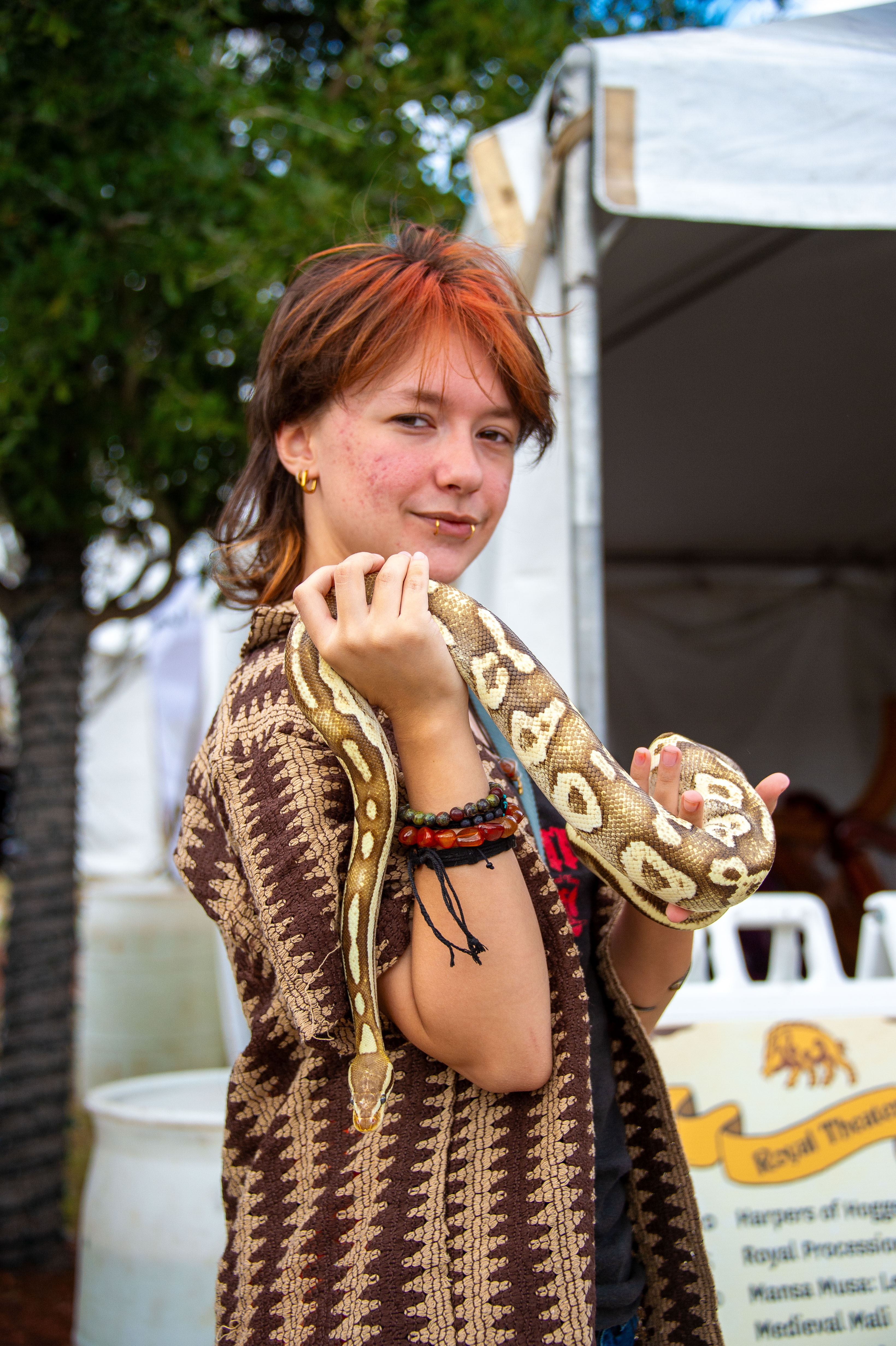 A person with multiple piercings holding up a large snake to the camera