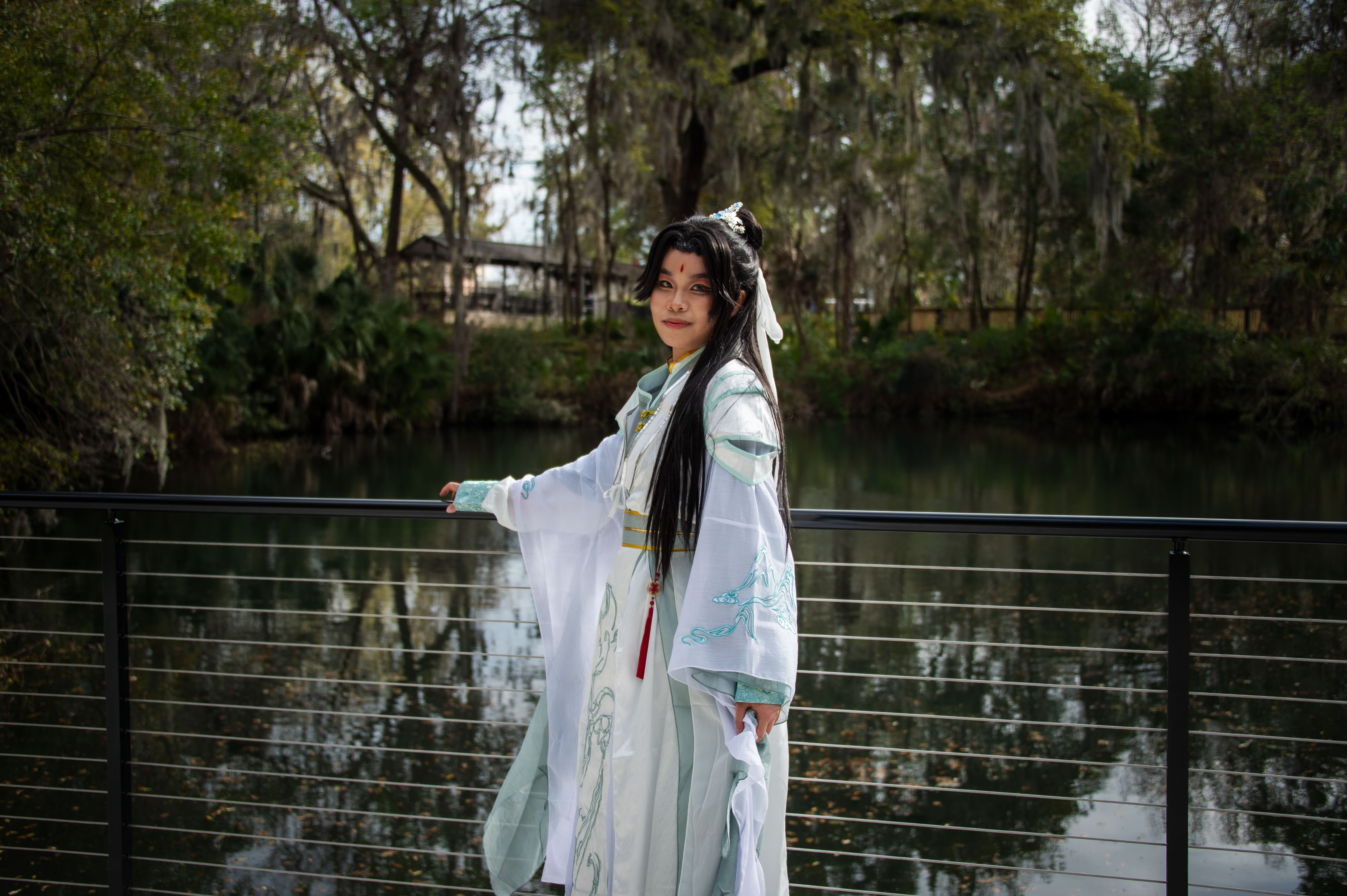 A person in cosplay standing by a railing over a small body of water.